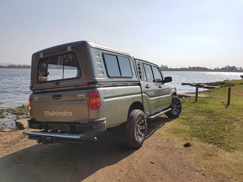 Mahindra double cab with a colour-matched canopy parked at the water's edge.