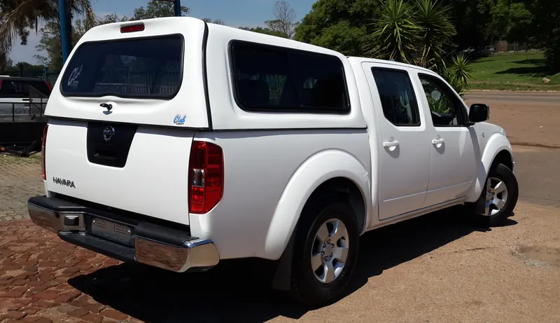 White Nissan Navara double cab with canopy, rear view showing the brake light.
